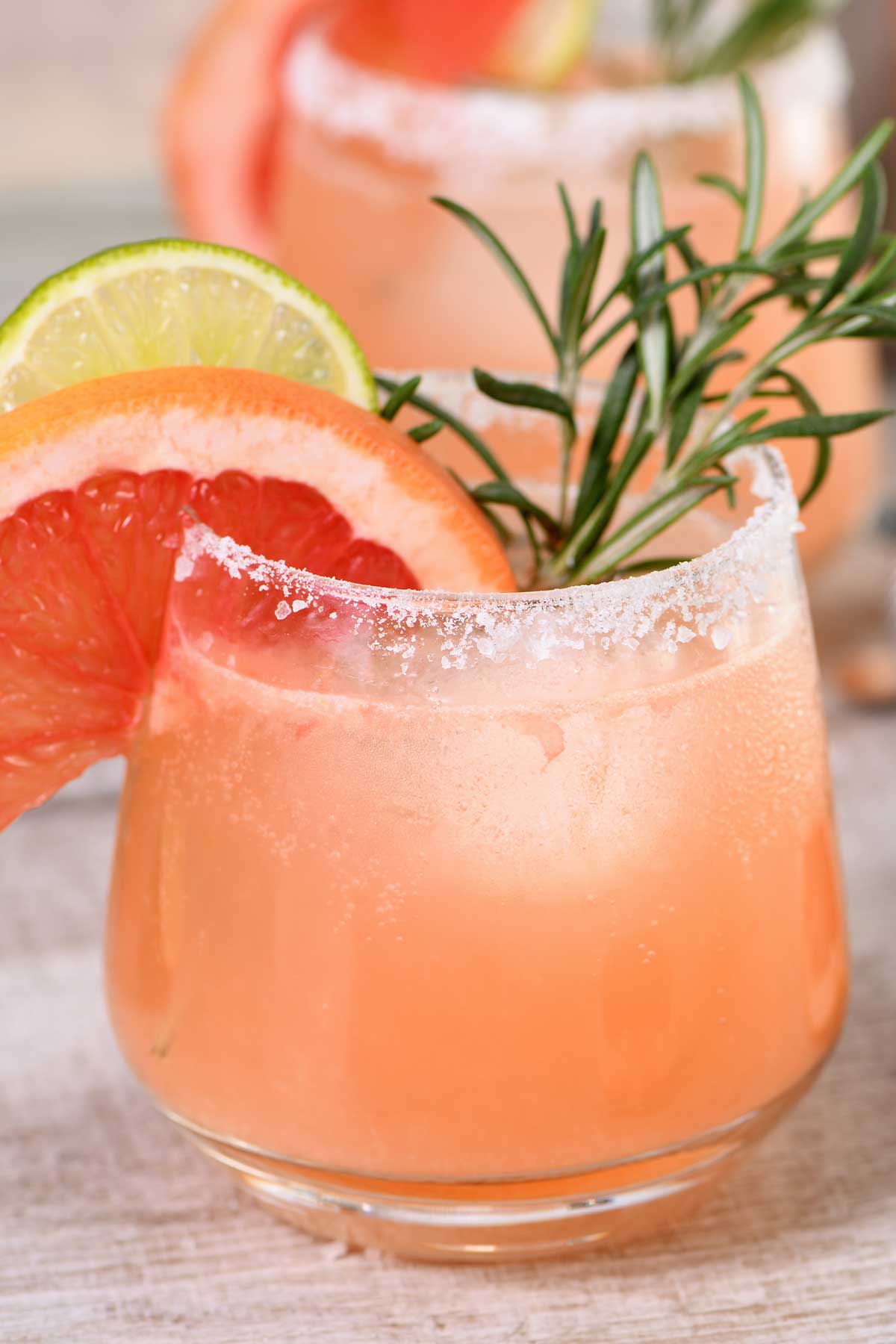 Paloma cocktail with salted rim, fresh grapefruit slice, lime wheel, and rosemary garnish